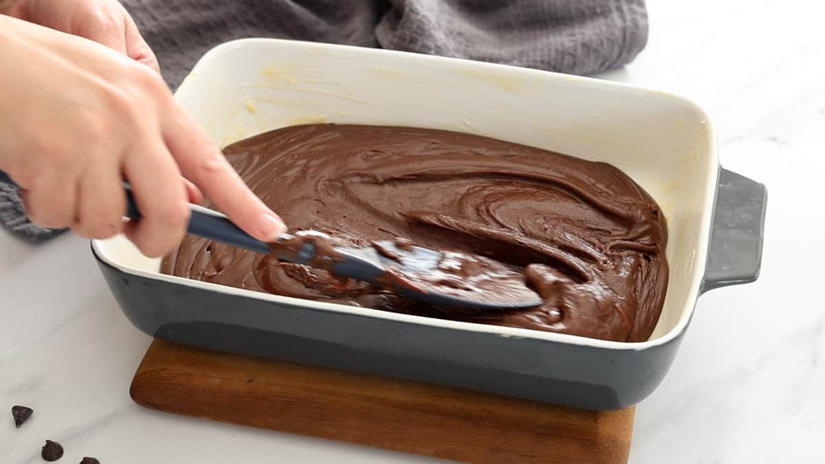 a blue spatula smoothing fudge in a ceramic baking dish.