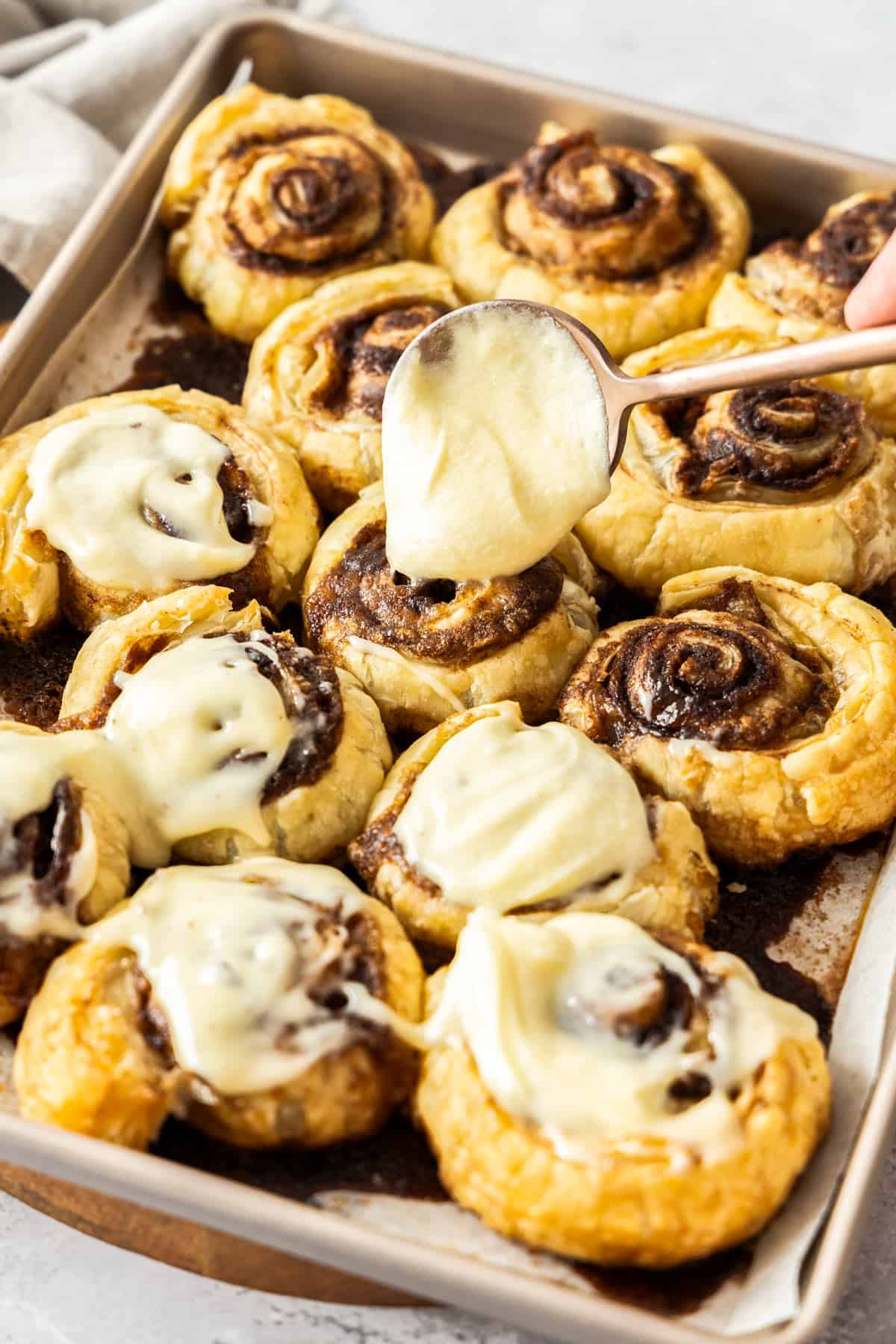 a spoonful of frosting hovering over a pan of cinnamon scrolls.