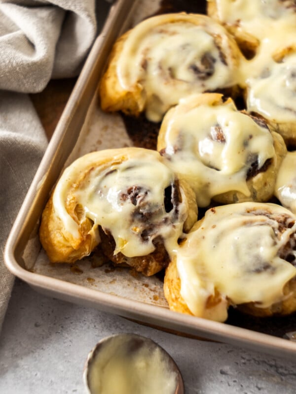 puff pastry cinnamon rolls in a metal pan, topped with frosting.