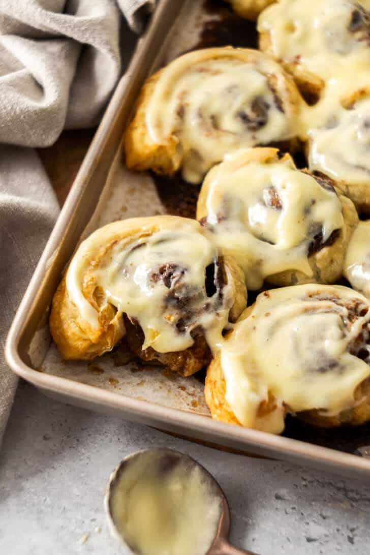 puff pastry cinnamon rolls in a metal pan, topped with frosting.