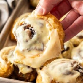 a hand holding cinnamon rolls in a pan.