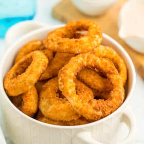 A white bowl stacked with air fryer onion rings.