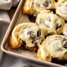 puff pastry cinnamon rolls in a metal pan, topped with frosting.