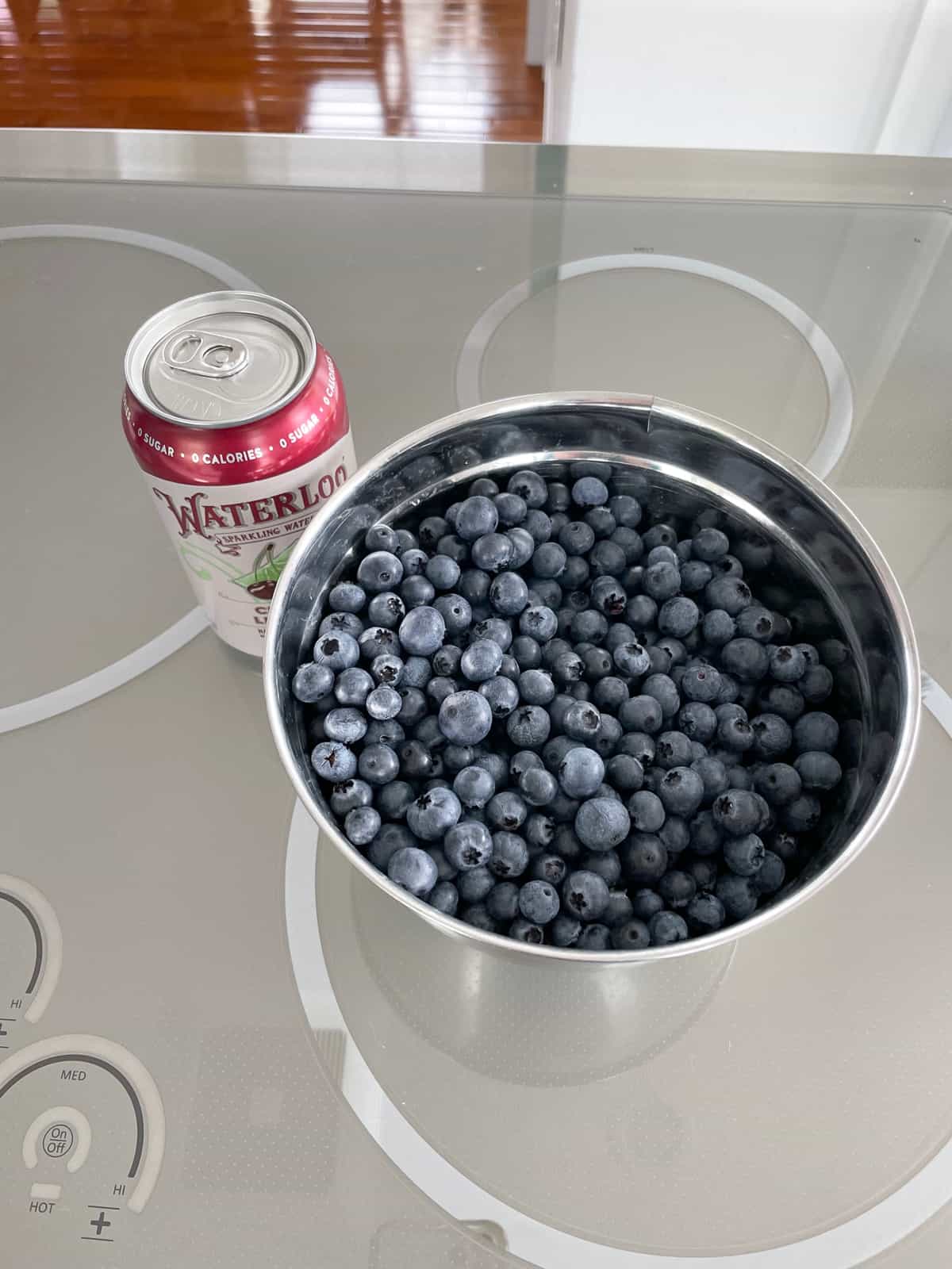a bowl of blueberries next to a can of sparkling water.