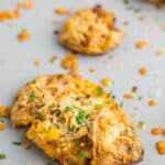 smashed fingerling topped with melted cheese and diced parsley potatoes on a baking sheet.