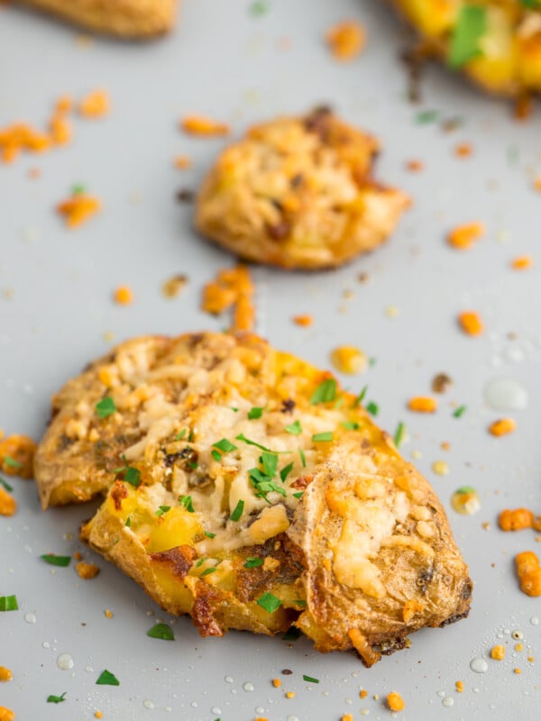 smashed fingerling topped with melted cheese and diced parsley potatoes on a baking sheet.