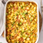 a white baking dish with a ham and potato casserole topped with sliced green onions.