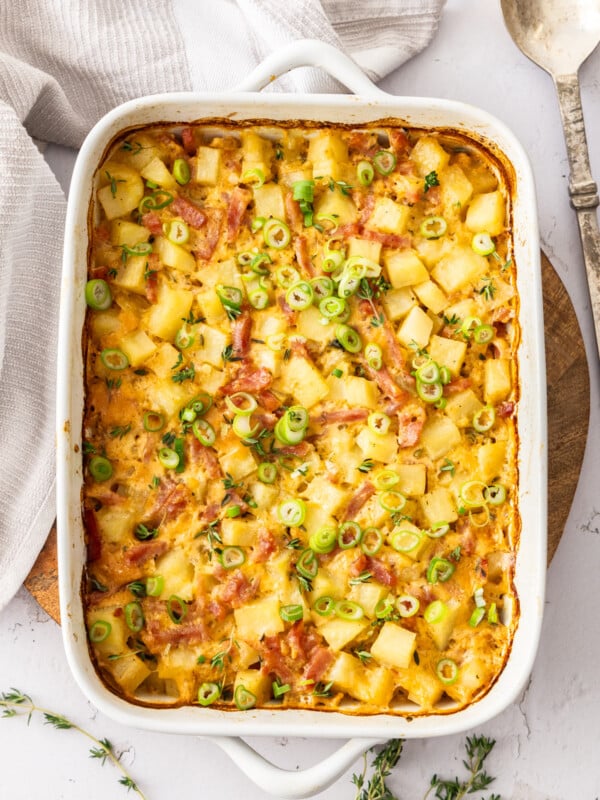 a white baking dish with a ham and potato casserole topped with sliced green onions.