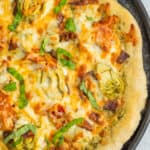 An homemade pizza on a cast iron pan topped with basil, artichoke hearts, and melted cheese.