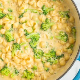 a teal cast iron dutch oven full of creamy mac and cheese with broccoli florets.