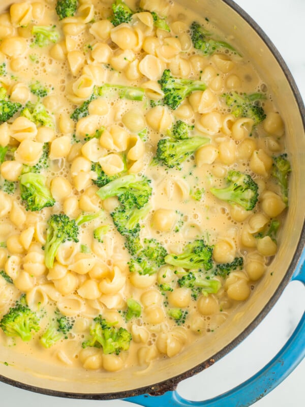 a teal cast iron dutch oven full of creamy mac and cheese with broccoli florets.