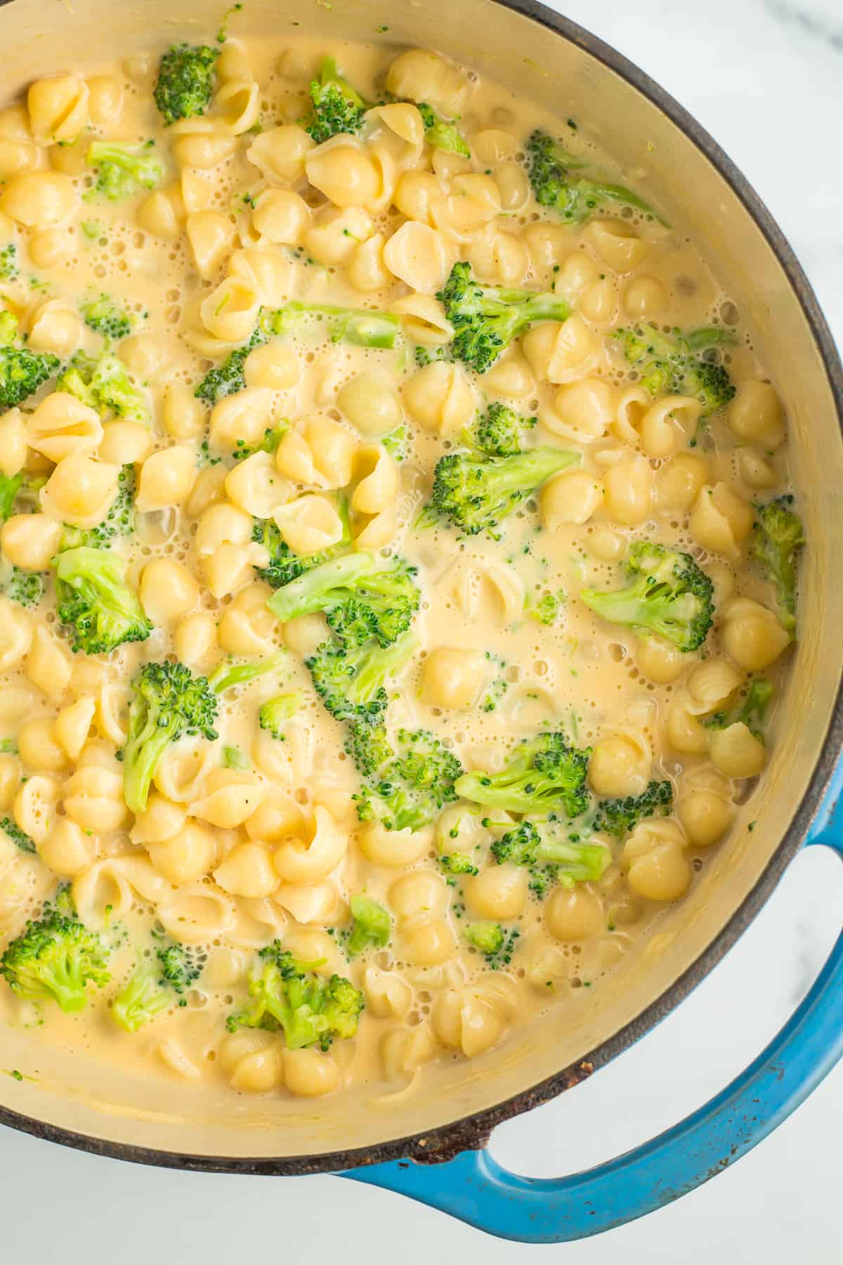 a teal cast iron dutch oven full of creamy mac and cheese with broccoli florets.
