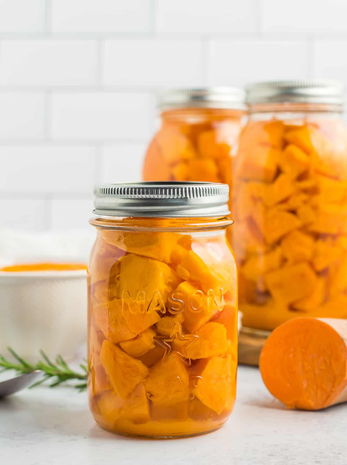 3 jars of canned sweet potatoes with rosemary on a white board.