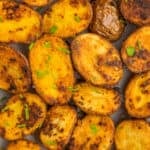 Roasted garlic potatoes on a baking sheet topped with chopped parsley.