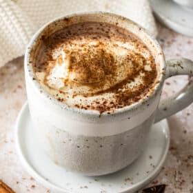 a grey speckled mug of slow cooker hot chocolate topped with whipped cream and cocoa.