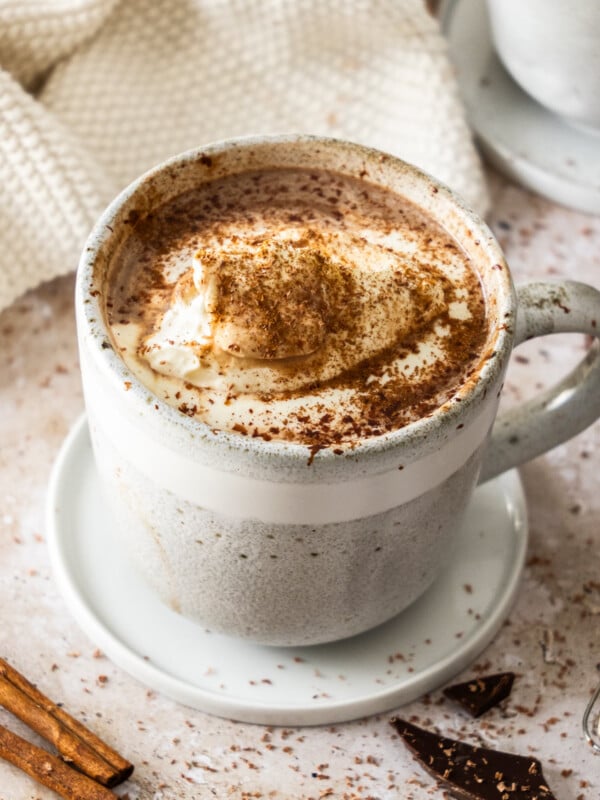 a grey speckled mug of slow cooker hot chocolate topped with whipped cream and cocoa.