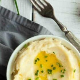 a white bowl with mashed potatoes topped with butter and chives.