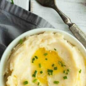 a white bowl with mashed potatoes topped with butter and chives.