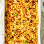A hashbrown breakfast casserole topped with bacon and sliced green onions in a white baking dish.