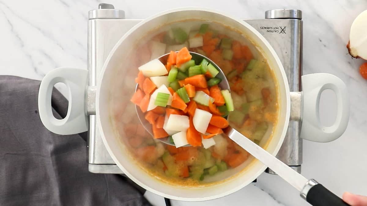 chopped vegetables in a ladle over a white saucepan.