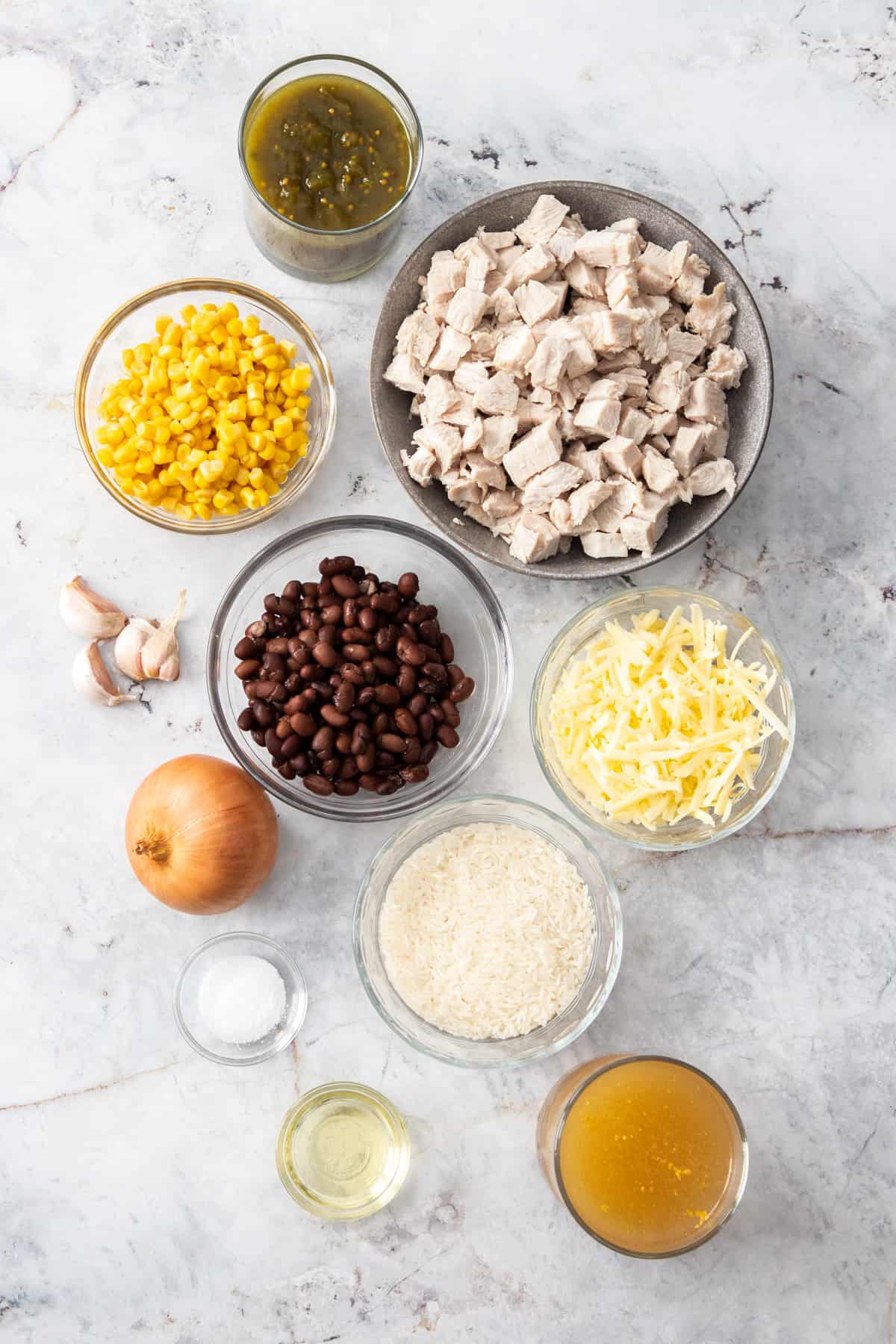 bowls of carrots, salsa, turkey, black beans, uncooked rice, and other ingredients on a marbled board.