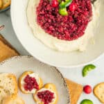 a white bowl with cranberry jalapeño dip with crackers and dip on a plate.