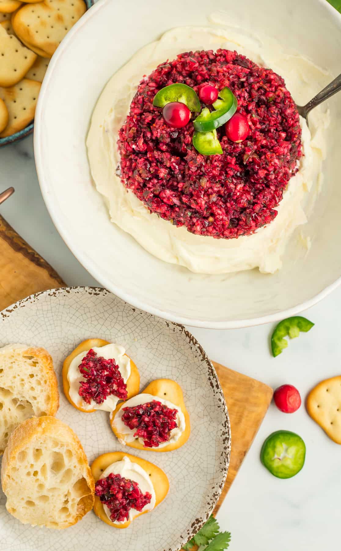 a white bowl with cranberry jalapeño dip with crackers and dip on a plate.