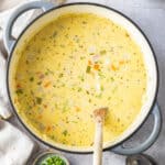 a large stockpot of ham and potato soup with a wooden spoon in it.