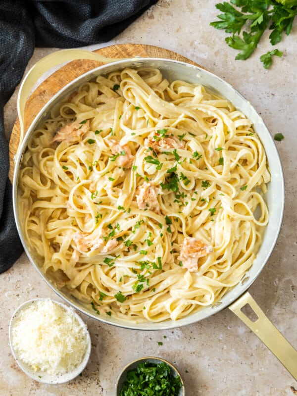 a white skillet with creamy smoked salmon pasta topped with chopped parsley.