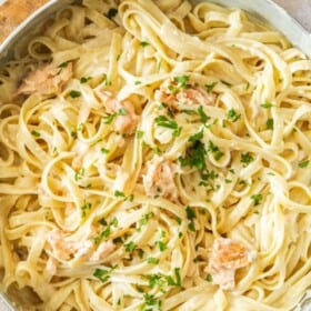 a white skillet with creamy smoked salmon pasta topped with chopped parsley.