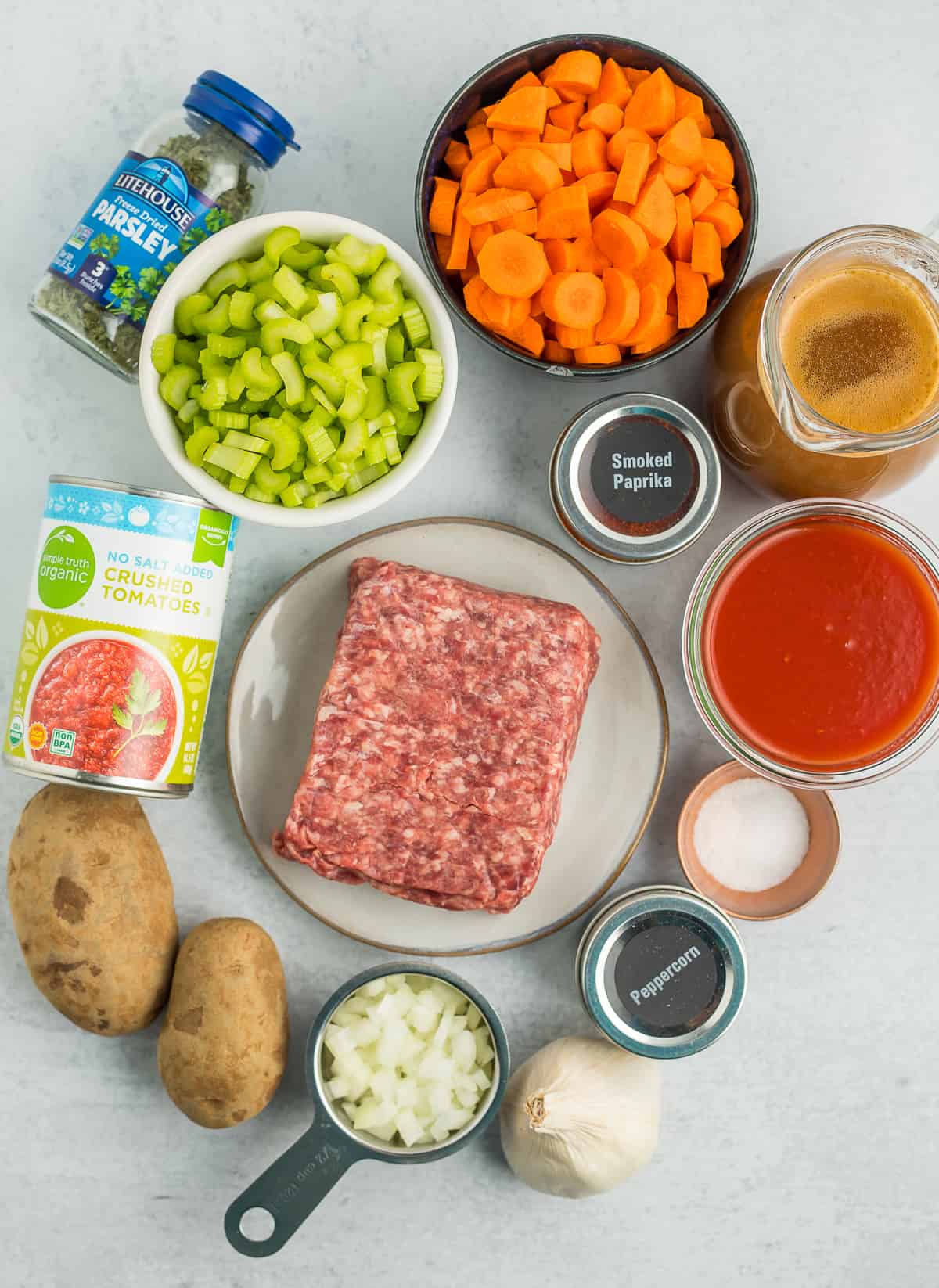 carrots, potato, onion, celery, burger, and other ingredients on a grey board.