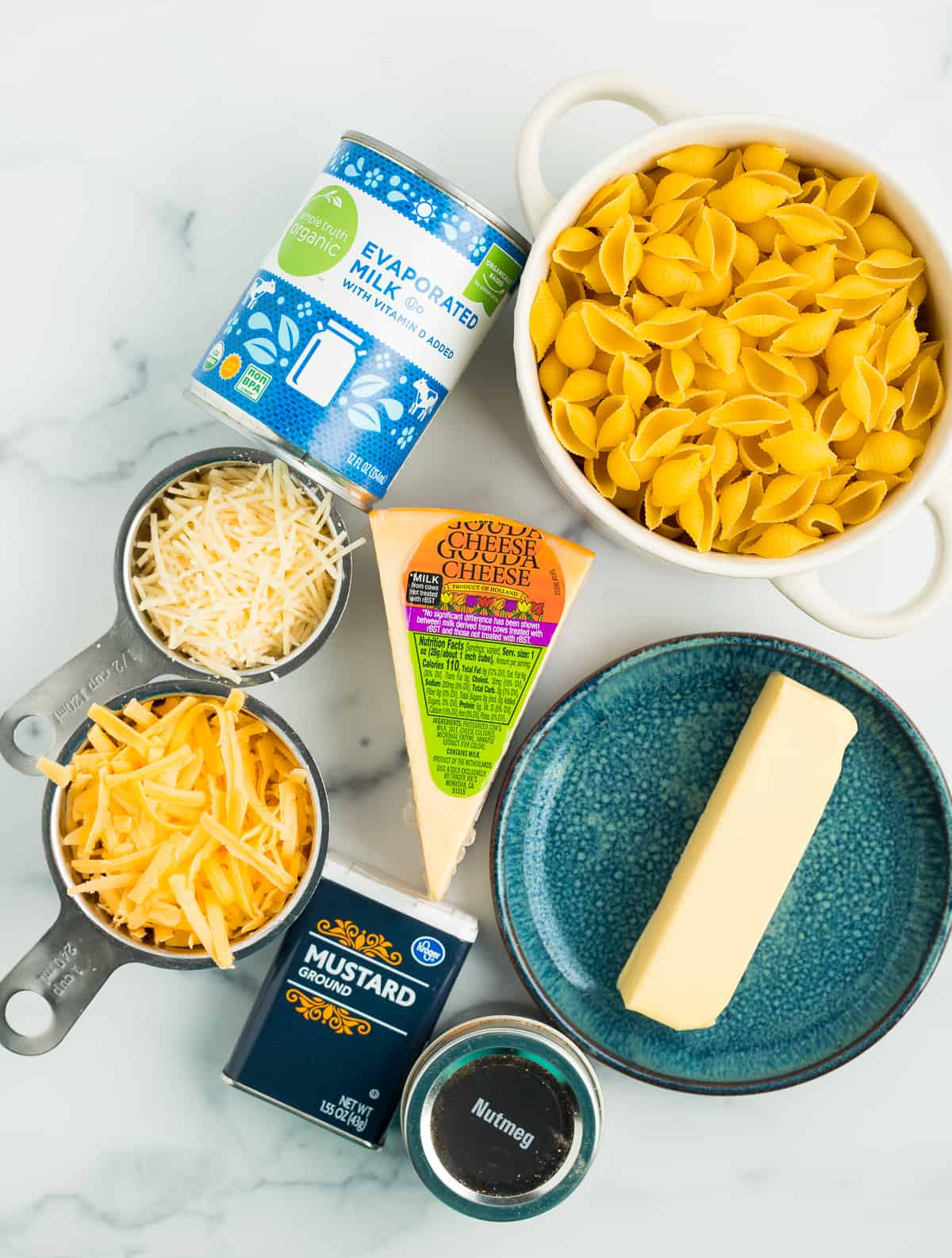 evaporated milk, shells, shredded cheese, butter, and other ingredients on a marbled board.