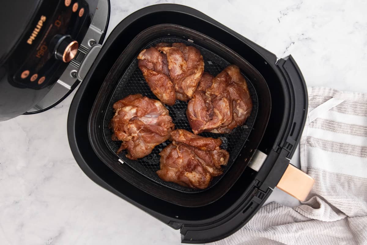 an air fryer basket with uncooked chicken thighs.
