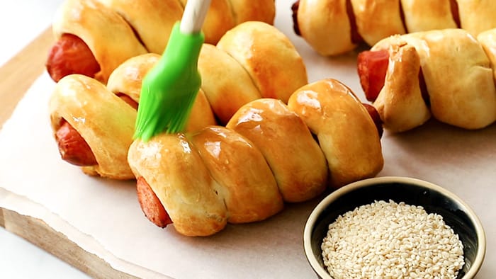 a silicone pastry brush brushing butter on a pastry wrapped hot dog.