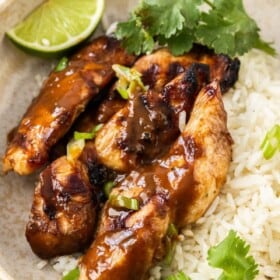 a beige bowl with rice, grilled chicken, cilantro, and lime wedges.