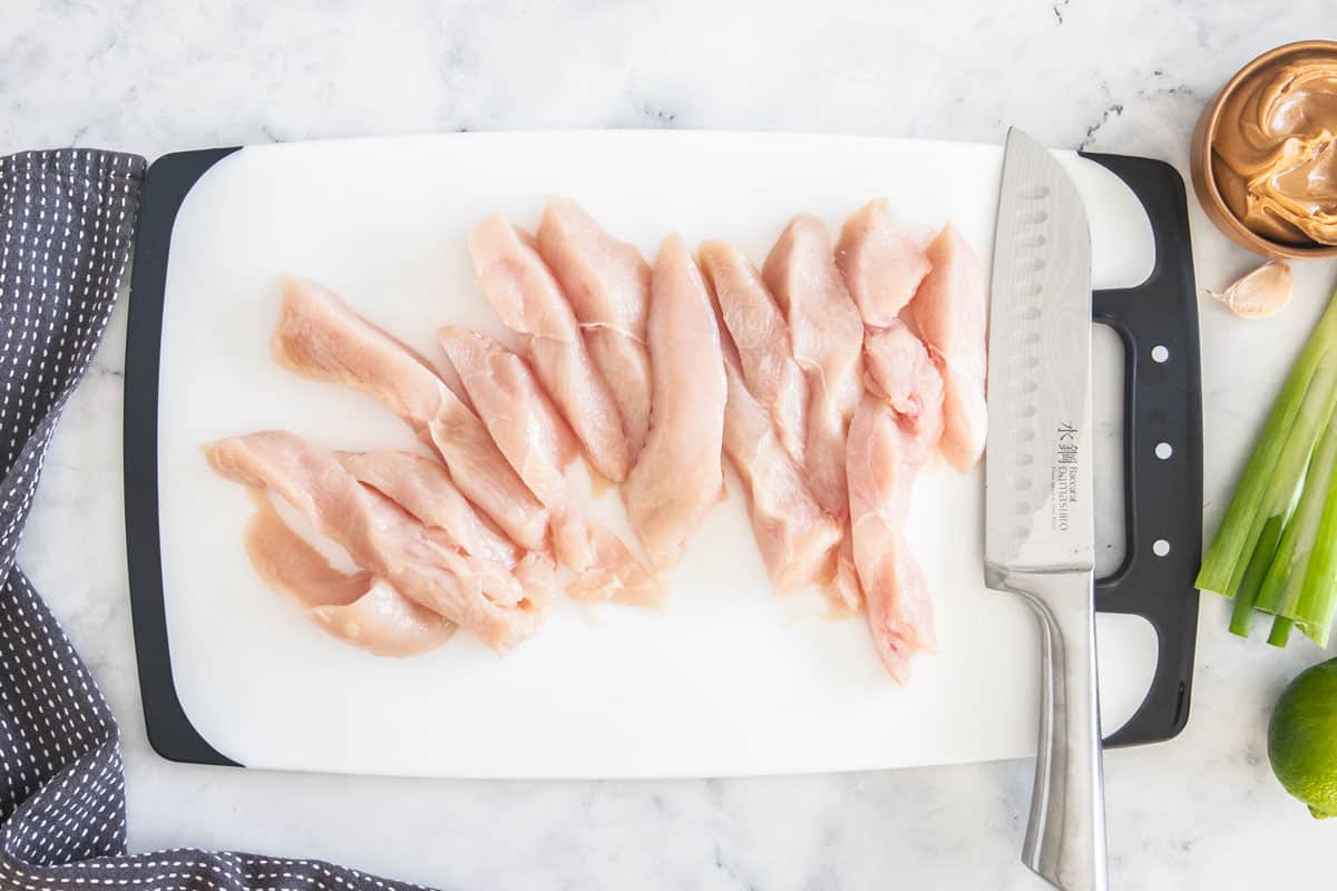 slices of uncooked chicken breast on a cutting board with a knife.