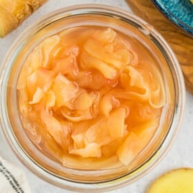 a glass jar of pickled ginger, with slices of ginger on a white board.