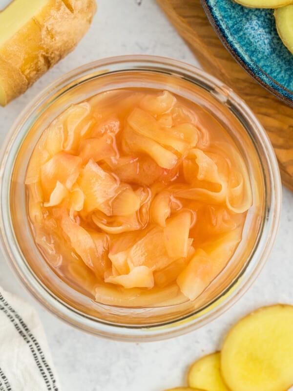 a glass jar of pickled ginger, with slices of ginger on a white board.