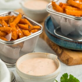 two bins of sweet potato fries and two small bowls with dipping sauce.