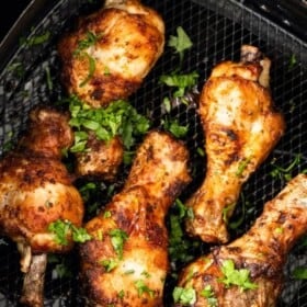 cooked drumsticks sitting in an air fryer basket topped with parsley.