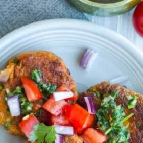 a plate of salmon cakes topped with chopped onions and tomatoes, and a small dish of chimichurri sauce.