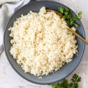 a grey bowl with Instant Pot basmati rice with a gold spoon and parsley on the side.