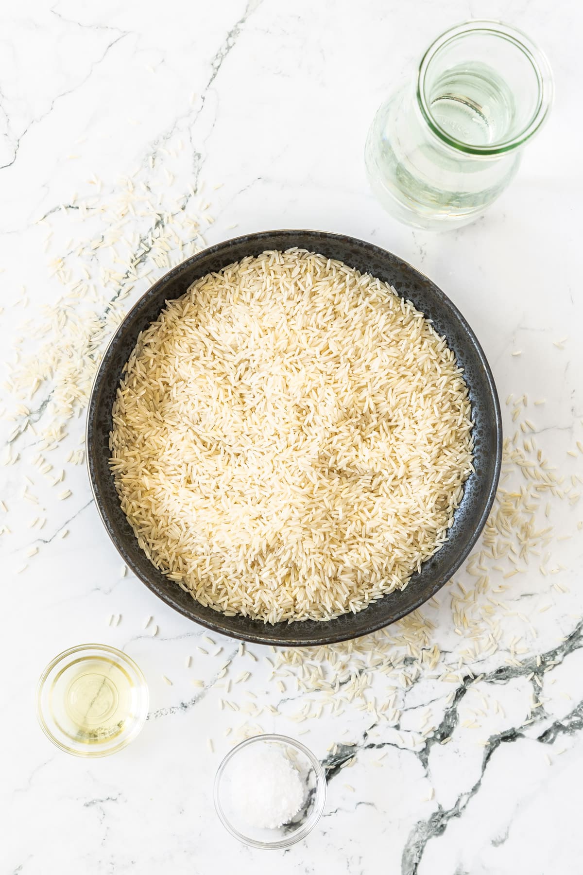 basmati rice in a dark bowl with water, salt, and oil in small bowls.