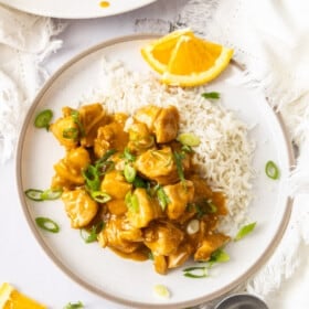 a plate of Instant Pot orange chicken with rice and slices of oranges and green onions.