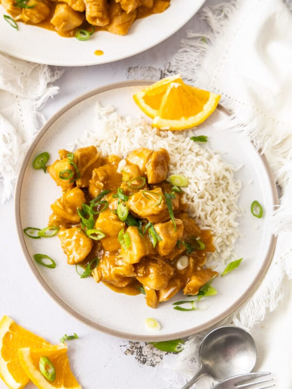 a plate of Instant Pot orange chicken with rice and slices of oranges and green onions.