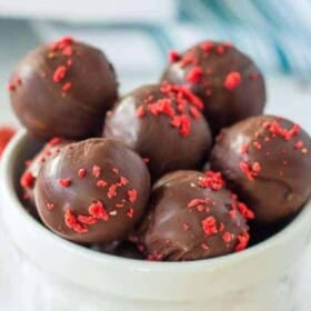 a white bowl of vegan chocolate truffles topped with freeze-dried strawberries.