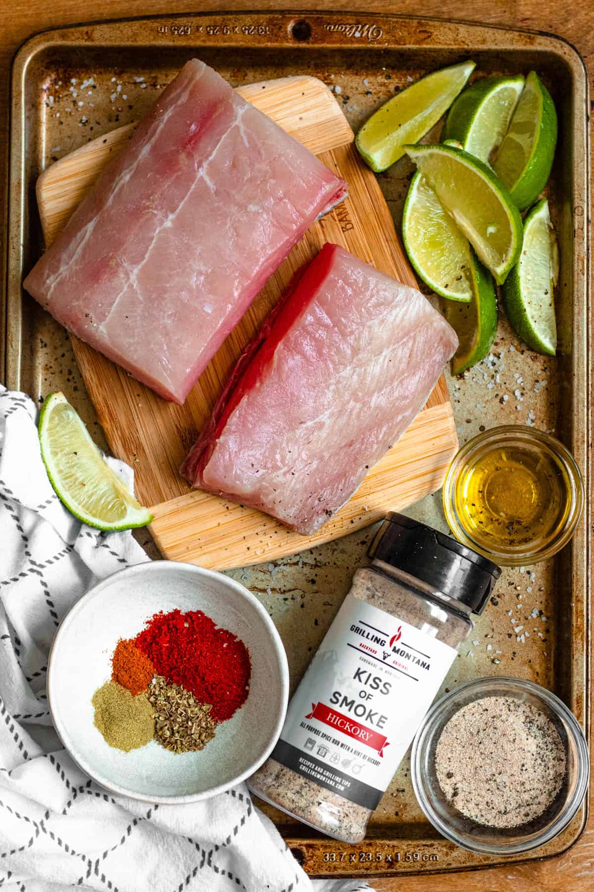 ingredients for blackened mahi mahi on a cutting board with limes, seasoning, olive oil, and a bottle of kiss of smoke.