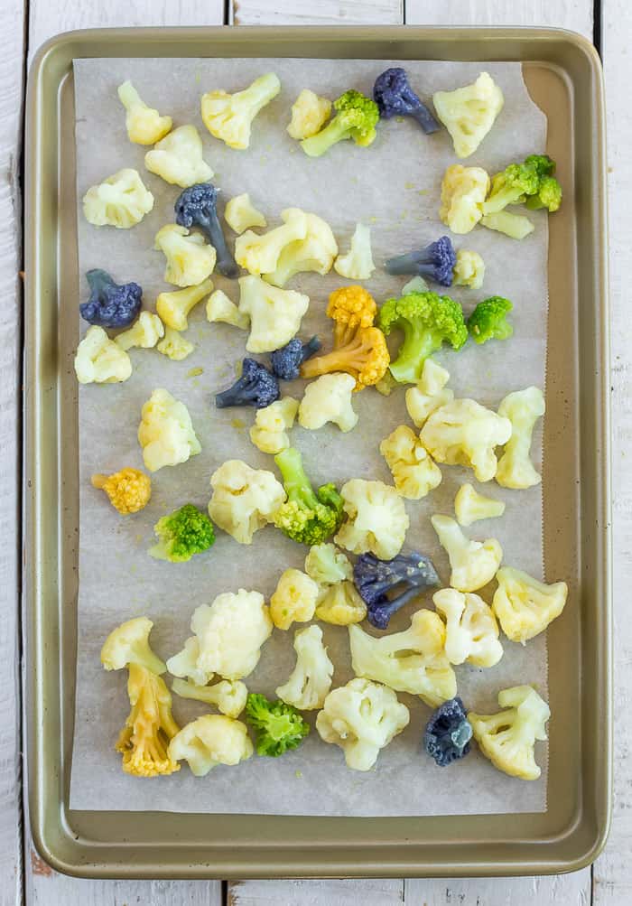 A baking sheet lined with parchment and colorful cauliflower florets.
