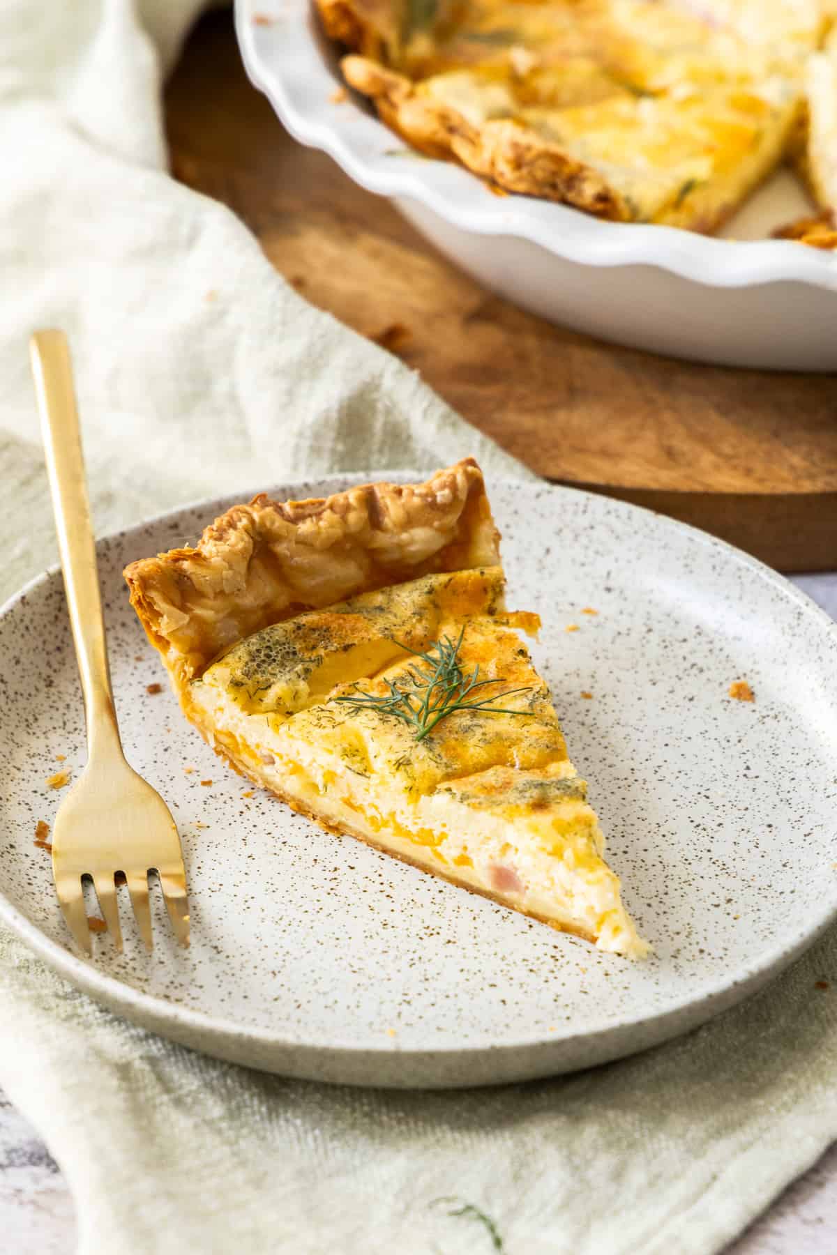 a slice of quiche on a plate with a gold fork.