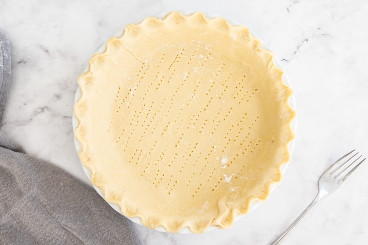 An unbaked pie crust in a pie plate with fork marks all over it.